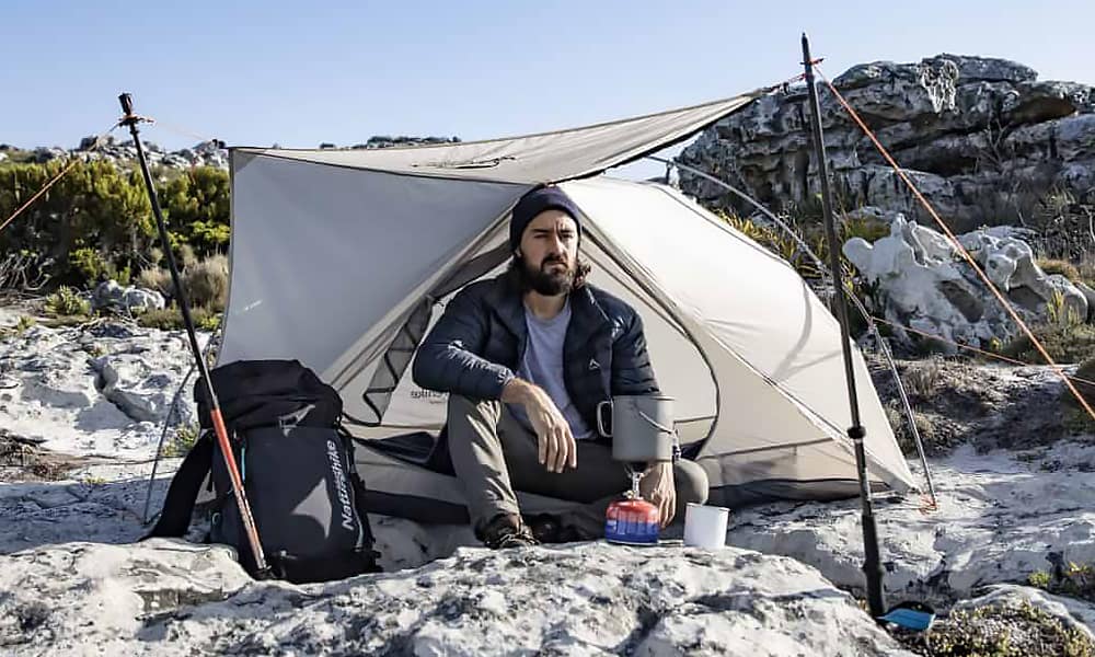 mies istuu teltan äärellä tekemässä ruokaa retkikeittimellä