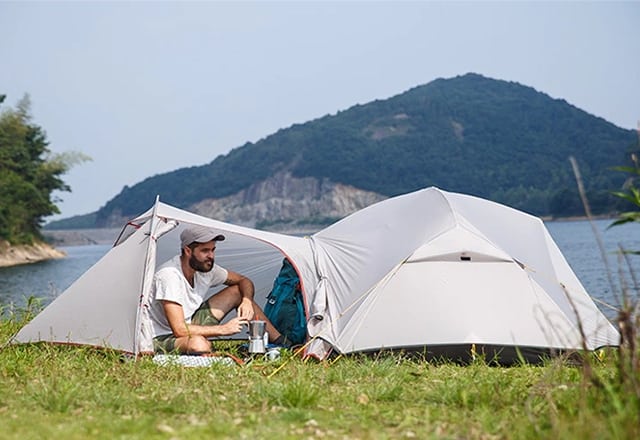 Mies istuu nurmikolla nylon -telttakangas teltassa